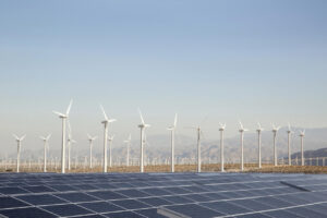 Many wind turbines and a large solar panel array in a desert valley, mountains in the distance and blue sky above. Palm Springs, California, USA